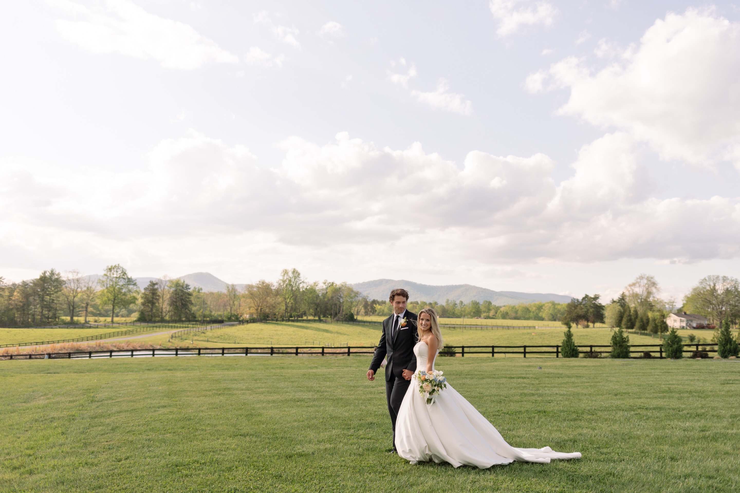 A couple walking across the pasture, the pond and the Blue Ridge behind them under a wide sky